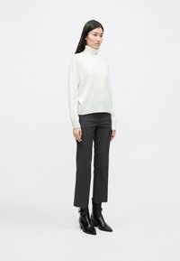 Λευκό πουλόβερ με ψηλό λαιμό, ριγωτή υφή, σε συνδυασμό με σκούρες γκρι κοντές παντελόνες; Το μοντέλο φ�ορά μαύρες μπότες μέχρι τον αστράγαλο με μυτερές μύτες.