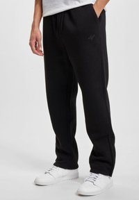 Svart joggebukse med avslappet passform, laget av mykt materiale. Har sidelommer og en subtil logo på låret. Kombinert med hvite joggesko.