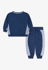 Παιδικό σετ φόρμας σε ναυτικό μπλε χρώμα με μπλούζα τύπου πουλόβερ που έχει ανοιχτογκρι πλαϊνές λεπτομέρειες, και παντελόνι που ταιριάζει με ελαστικά μανσέτες και μέση.