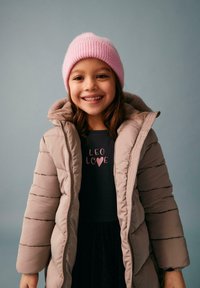 Beżowa kurtka puchowa z futrzanym kapturem, noszona na ciemnej bluzie z napisem "LEO LOVE" w różowym kolorze. Jasnoróżowa czapka z prążkowanego materiału.