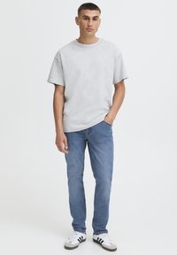 Tricou din bumbac gri deschis cu decolteu rotund, asortat cu blugi din denim albastru. Ținuta este completată de adidași albi și gri cu accente negre.