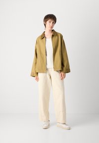 Olive green lightweight jacket with a collar, paired with a white shirt and cream wide-leg pants. White sneakers complete the outfit.