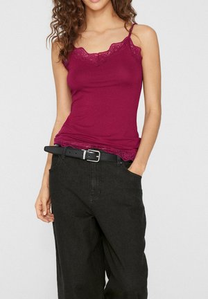 Femme portant un caraco ajusté rose foncé bordé de dentelle, rentré dans un pantalon noir ample taille haute avec une ceinture noire.