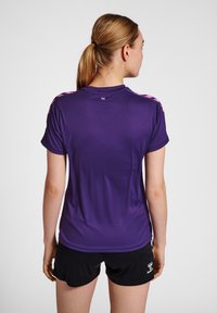 Lilla træningsskjorte med korte ærmer, der har lyserøde detaljer på skuldrene og et glat, let stof. Sammen med sorte shorts.