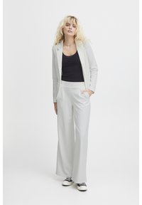 Hellgrauer, taillierter Blazer und passende weit geschnittene Hose, kombiniert mit einem schwarzen Tanktop und schwarz-weißen Sneakern. Glatte Stoffstruktur.