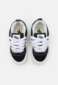 Adidași alb-negru cu un superior din nabuc și pânză, având un design alb cu șireturi, guler căptușit și logo pe limbă.