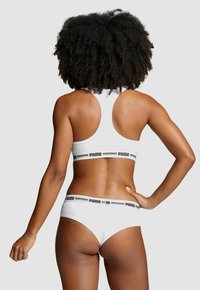 Weißes sportliches Bralette und passende Unterhose mit einem schwarzen Logo-Band. Glatte Textur, Racerback-Design und mittelhohe Passform.