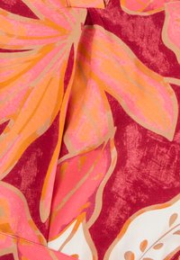 Tissu à manches courtes présentant de grands motifs floraux roses et orange sur un fond rouge profond, avec une texture subtile et des détails de couture visibles.