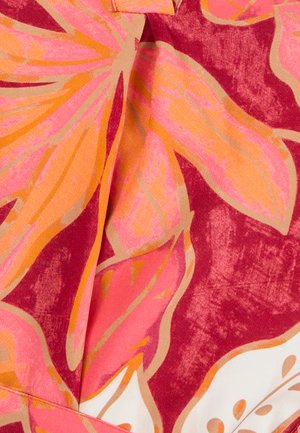 Tela de manga corta con grandes patrones florales en rosa y naranja sobre un fondo rojo intenso, con una textura sutil y detalles de costura visibles.