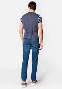 Granatowa kamizelka w kratę związywana z tyłu, noszona na paskowanej koszulce z krótkim rękawem; połączona z niebieskimi dżinsami i szarymi sneakersami.