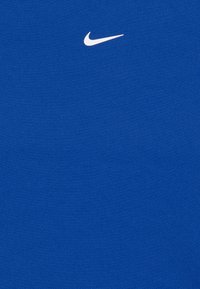 Blå atletisk t-shirt lavet af åndbart stof, med et hvidt Nike swoosh-logo placeret øverst til venstre.