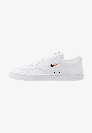 Biały niski sneaker Nike z teksturowanej skóry, z przodu na sznurowadła, z czarno-pomarańczowym haftowanym logo po boku, pokazany z boku.