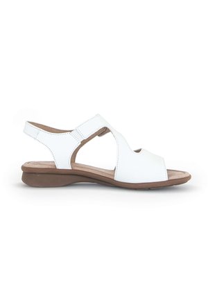 Sandale en cuir blanc avec une semelle brune basse, présentant une ouverture à l'avant, un design entrecroisé et une sangle ajustable à la cheville. Texture lisse.