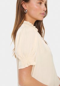 Blouse met pofmouwen in een crèmekleurige stof met een gerimpelde halslijn en elastische manchetten, met een soepele structuur en een ontspannen silhouet.
