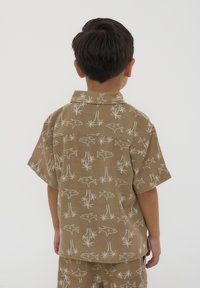 Camicia a maniche corte in tessuto marrone chiaro con motivi di squali e piante bianchi. Presenta un colletto e una vestibilità rilassata per il massimo comfort.