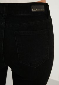 Crne traperice od denima s klasičnim dizajnom s pet džepova. Sadrže oznaku LELA DENIM PROJECT, glatku teksturu i kroj s prilagodljivim fit.