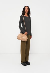 Langarmige donkergrijze top, olijfgroene wijde broek, zwarte plateau-schoenen en een beige geplisseerde handtas met een schouderband.