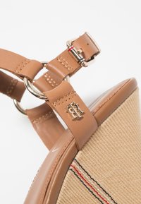 Sandale plateforme beige avec un dessus en toile tissée, une bride à boucle, des accents en matériel doré et un motif de couture multicolore subtil.