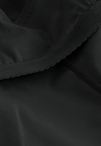 Zwart sportkledingstof met een gladde textuur, een aansluitende pasvorm en een afgewerkte rand. Inclusief naden en een zachte kraagdetail.