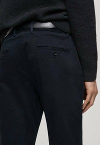 Pantaloni bleumarin cu o textură fină, având două buzunare la spate și un închidere cu un singurbuton. Purtați cu un pulover negru texturat.