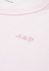 Lichtroze katoenen t-shirt met een geribbelde ronde hals en een geborduurd "A&B" logo in een iets donkerder roze. Zachte structuur.