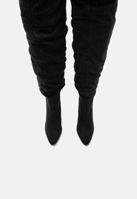 Spidse tå sorte ankelstøvler i blødt ruskind med hævet prikket tekstur og samlet look. Glat finish, slank hæl og minimalistisk design.