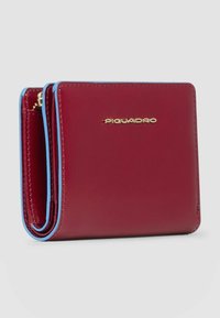 Bordeauxrode leren portemonnee met blauwe accenten, een compact drieluiksontwerp en gouden logodetail op de voorkant. Heeft een gladde textuur.