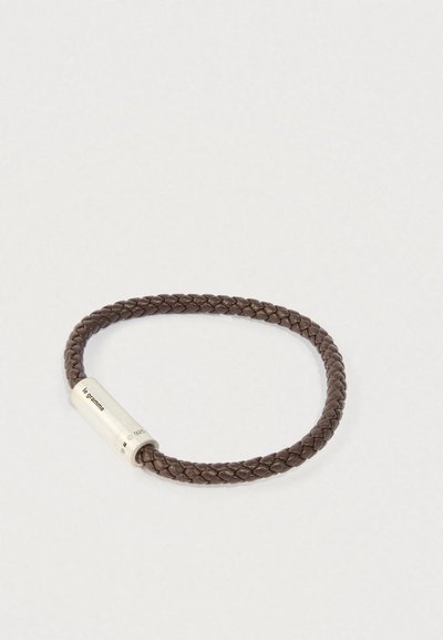 Brūns pītā ādas rokassprādze ar cilindrisku sudraba aizdari, uz kuras ir iegravēts "le gramme" un "925" atzīmes.