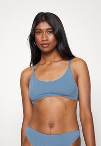 Top de biquíni texturizado azul com decote em forma de scoop, alças finas ajustáveis e acabamento suave. Combinado com parte de baixo de biquíni correspondente.