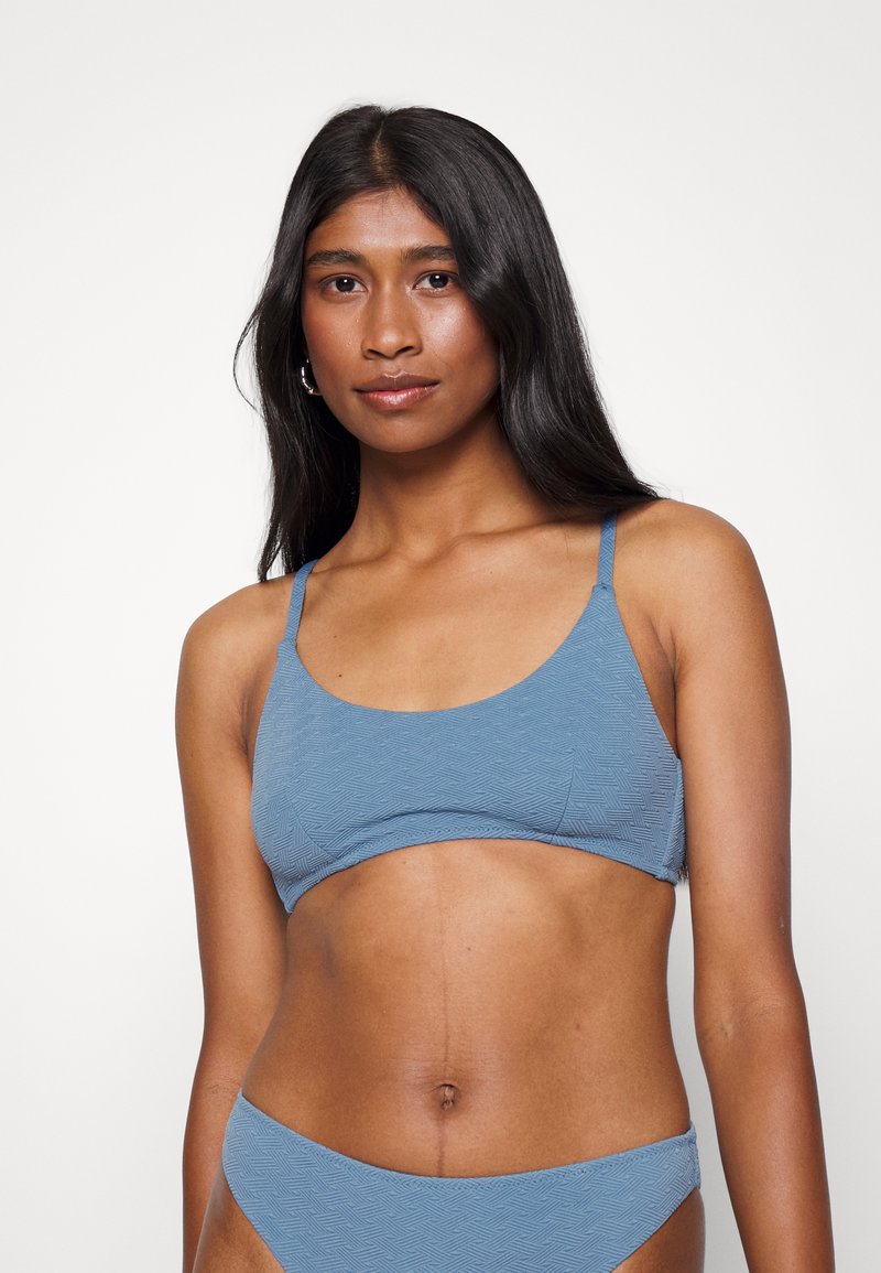 Top de biquíni texturizado azul com decote em forma de scoop, alças finas ajustáveis e acabamento suave. Combinado com parte de baixo de biquíni correspondente.