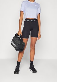 Camiseta corta de color púrpura claro, pantalones cortos negros de cintura alta, zapatillas deportivas negras, bolsa de deporte negra con marca blanca. Textura de tela suave.