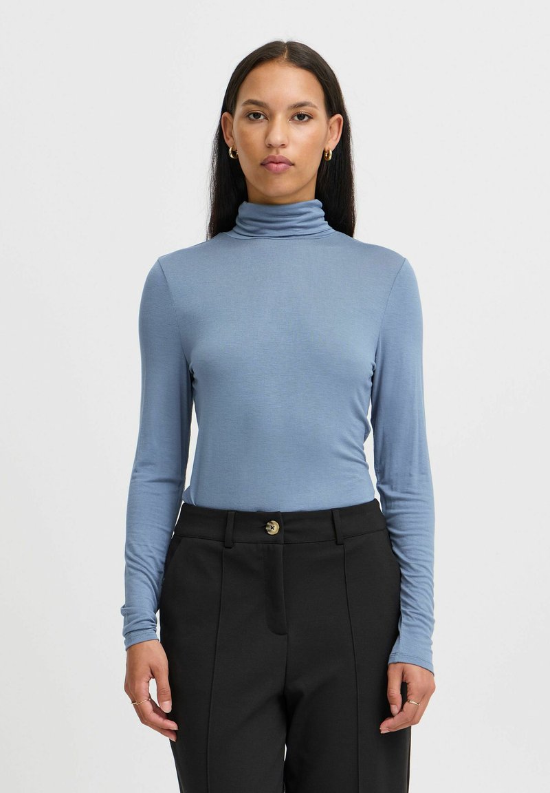 Helles blaues Longsleeve-Merchandise mit engen Schnitt, kombiniert mit hochtaillierten schwarzen Hosen mit Knopfverschluss und Seitentaschen.