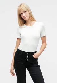 T-shirt blanc à manches courtes côtelée, associé à un jean noir taille haute avec des boutons argentés en guise d'accents et des poches avant. Texture de tissu lisse.