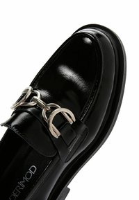 Black patent leather loafers feature a rounded toe, silver buckle accent, and flat rubber sole. The design includes a textured finish.