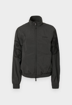 Schwarze leichte Jacke mit Stehkragen, Reißverschluss vorne, elastischen Bündchen und dekorativer Stickerei an den Ärmeln. Glatte Stoffstruktur.