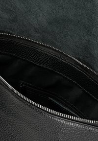 Vnitřek černé kožené tašky s texturovaným povrchem, vybavené zipovým uzávěrem a hladkým černým podšíváním. Obsahuje malou kapsu na zip.