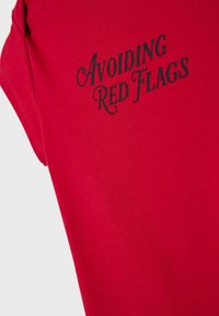 Tissu rouge avec texte noir "Éviter les signaux d'alarme" dans une police stylisée, affiché sur un vêtement plié.