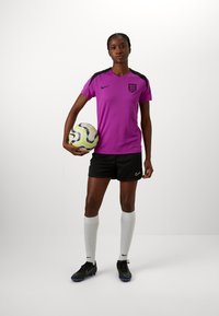 Pink Nike soccer jersey with black accents, black shorts, white knee-high socks, and black cleats holding a patterned soccer ball.
