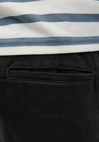 Czarne spodnie z tylną kieszenią, charakteryzujące się gładką fakturą. Pas jest częściowo widoczny, ukazując poziomo paskowaną niebiesko-białą koszulę.