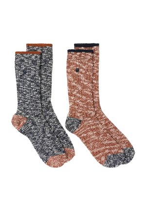 Two pairs of knitted crew socks, one black and white with rust accents, the other rust and white with black accents, laid flat on a white background.