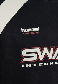 Black sportswear fabric with white and red text reading "hummel Sportswear" and partially visible "SWAN INTERNATIONAL" logo.