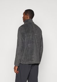 Γκρι φλις ζακέτα με ψηλό γιακά, υφασμάτινη υφή και χαλαρή εφαρμογή. Διαθέτει προσεγμένο φινίρισμα και διακριτική ραφή στην πλάτη.