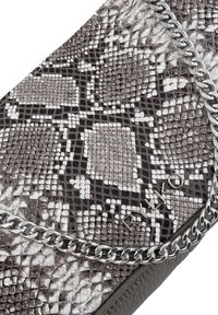 Sac à épaule texturé en imprimé serpent gris et noir, avec une bandoulière en chaîne argentée et un détail de logo. La base lisse et structurée contraste avec le motif.
