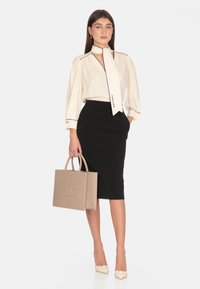 Blusa crema con colletto a fiocco, gonna a tubino nera, borsa strutturata beige e scarpe décolleté crema con decorazioni a fiocco.