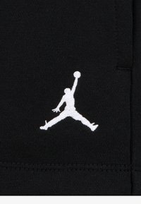 Fekete szövet, fehér hímzett Jumpman logóval, amely egy játékos sziluettjét ábrázolja dinamikus pózban. Egyszerű és letisztult design.