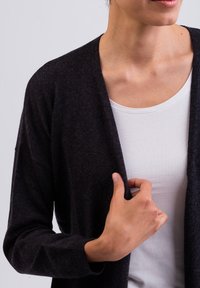 Cardigan grigio scuro realizzato in un tessuto morbido e testurizzato, con design aperto, indossato sopra una t-shirt bianca, caratterizzato da maniche lunghe e una vestibilità comoda.