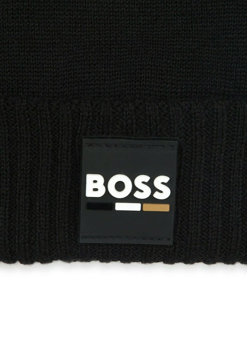 Bonnet en tricot noir présentant une texture côtelée et un patch rectangulaire noir avec le nom de la marque "BOSS" en blanc, noir et marron.