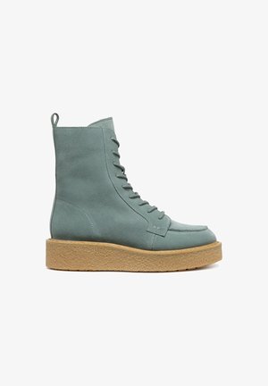 Bottines en suede bleu clair, avec un bout rond, un laçage à l'avant et une semelle texturée beige. Équipées d'une languette à l'arrière pour un enfilage facile.