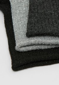 Drei übereinander gestapelte gestrickte Textilstücke in Schwarz, Silber und Grau. Jedes hat eine gerippte Textur mit einem Hauch von metallic Schimmer.