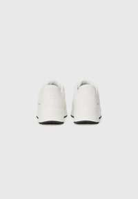 Des chaussures de sport blanches avec une tige synthétique lisse, un bout rond, un col rembourré et une semelle en caoutchouc noir avec des accents texturés.